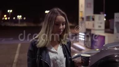 迷人的年轻女子打开车门，一边拿着一杯咖啡，坐在乘客座位上。 <strong>加油</strong>站